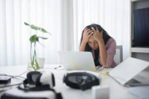 Stressad kvinna sitter vid skrivbord och tar sig för pannan