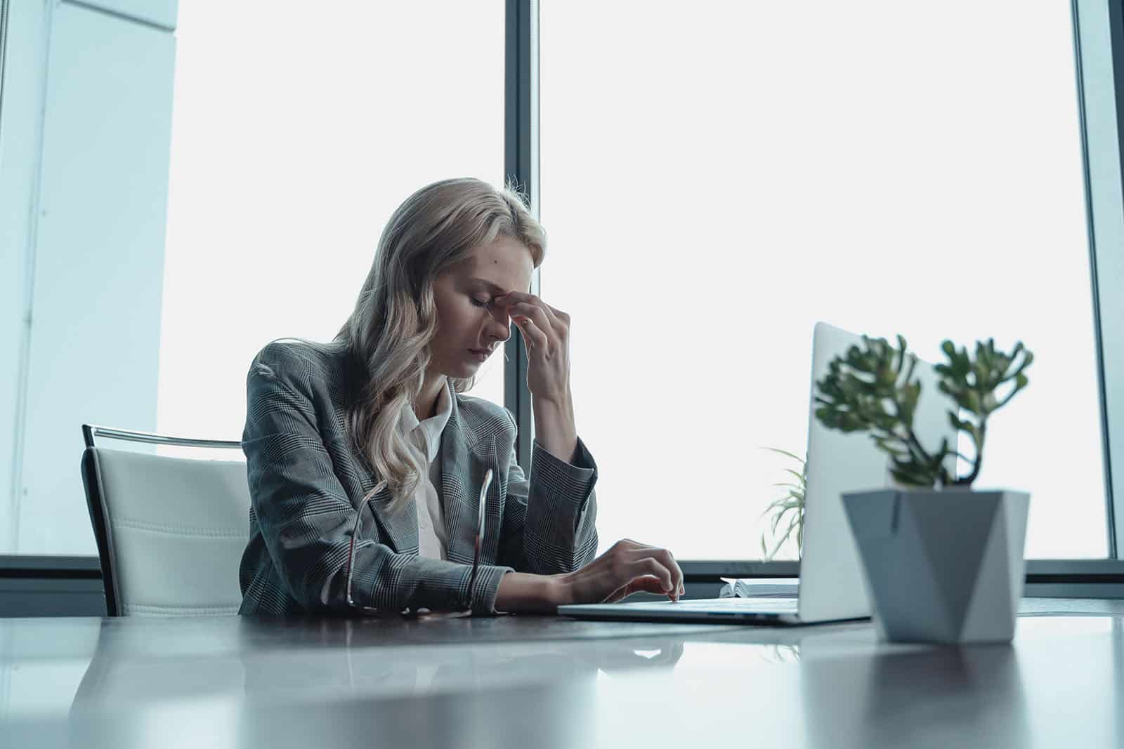 Stressad kvinna sitter vid skrivbord och tar sig för pannan