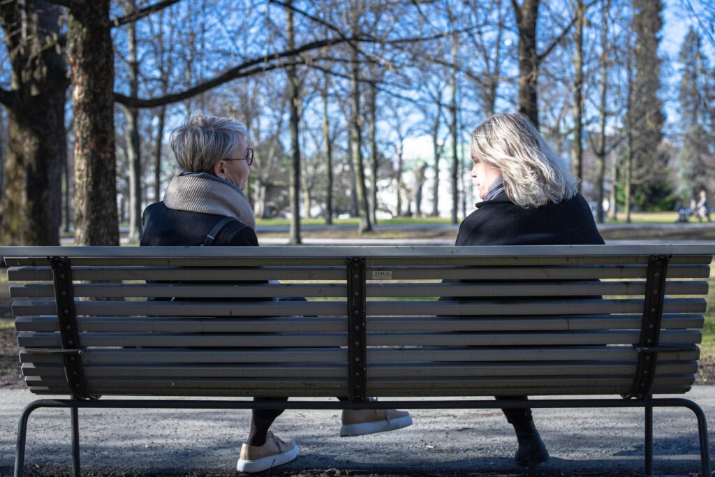 Två kvinnor som sitter på en bänk och pratar.